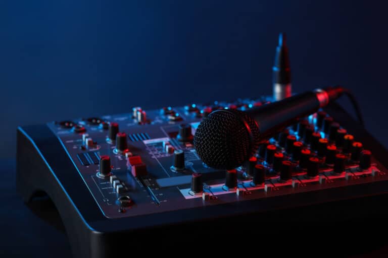 Professional mixing console with microphone on table against dark blue background, closeup